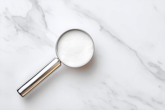 Top view of silver measuring scoop with white powder supplement for pets on marble background. Probiotics, calcium or vitamins powder for dogs and cats nutrition. Copy space.
