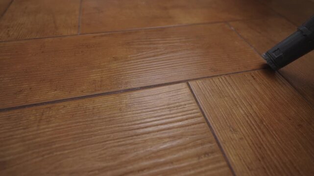 Vacuum cleaner nozzle working on parquet floor, thoroughly removing dust and dirt from between wooden planks, representing cleaning and maintenance activities. Concept of household chores, housework.