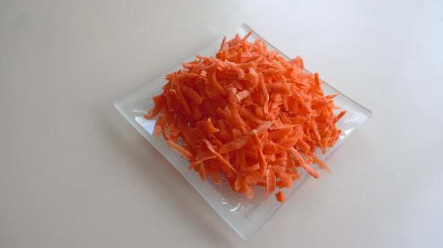 Grated carrots on a glass plate.
An appetizing pile of bright orange grated carrots is neatly laid out on a transparent glass plate on a light background, emphasizing freshness and natural color.