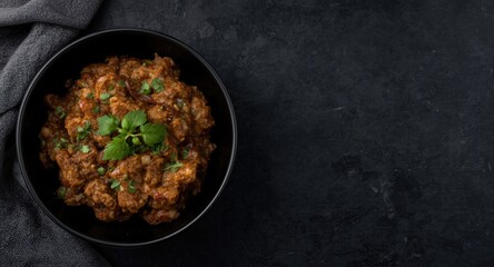 Mashed smoky eggplant bhurta served in black bowl over dark slate with empty copy space