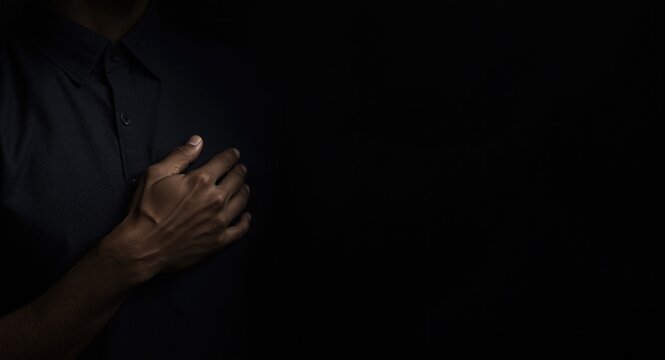 Male hand softly touching chest with dark backdrop and wide copy space illustrating intimate emotion and communicative openness