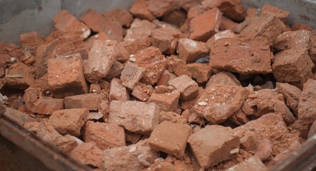 Fototapeta premium Close-up of red brick rubble in a metal waste container highlighting building demolition process