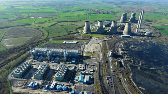 Aerial view of the West Burton Power Station, with its imposing cooling towers casting long shadows across the landscape, juxtaposed against the green fields, Retford, United Kingdom.