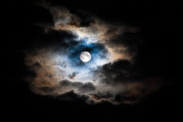 Fototapeta premium Full moon glowing brightly behind dramatic clouds at night