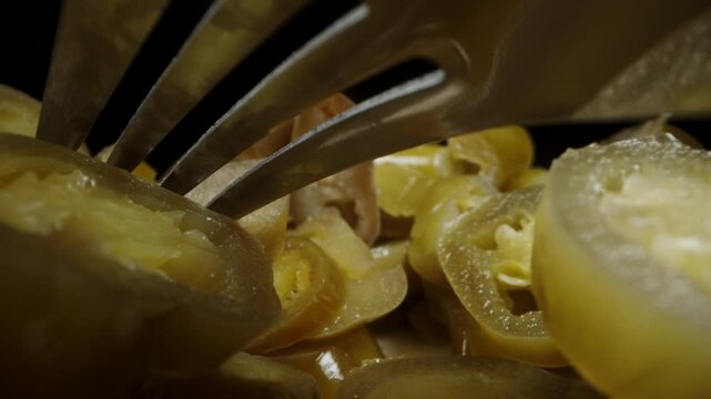 A fork is lying on a pile of sliced green Jalapeno peppers. The camera glides beneath it. Dolly slider extreme close-up.