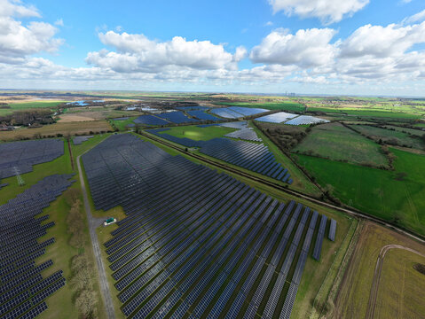Aerial view of solar panels glinting under the partly cloudy sky, juxtaposed with the green fields and distant buildings, Retford, United Kingdom.