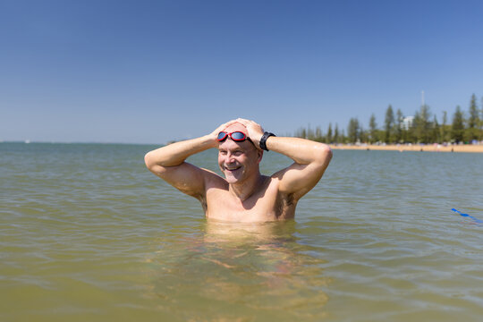 Male open water swimmer standing in water with hands on head smiling
