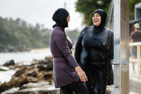 Women in burkinis under the pouring water from the beach shower near ocean pool