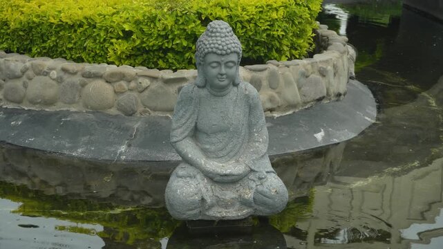 Siddartha Buddha meditating statue in the middle of a pond with many fish in the water. Located in "Parque Chino" in Miraflores district of Lima, Peru.