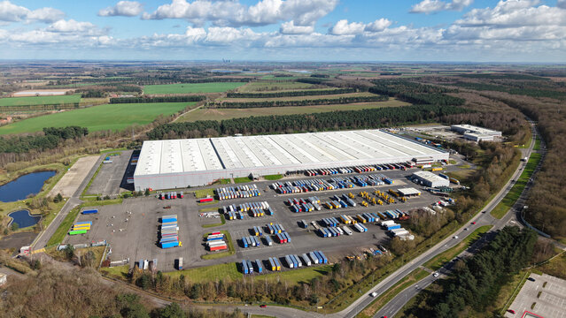 Aerial view of a vast distribution centre with rows of colourful shipping containers gleaming under the sun, surrounded by green fields, Worksop, England, United Kingdom.