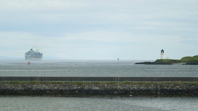Static shot of a cruise ship leaving port and a lighthouse in Stornoway.
