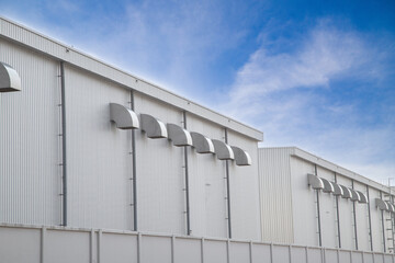 Obraz premium Rows of industrial ventilation ducts on a modern metal warehouse wall under blue sky.ndustrial air conditioning and ventilation system for energy-efficient factory building.