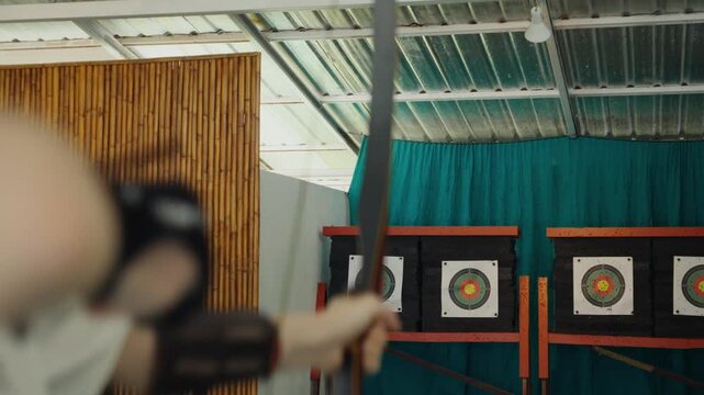 Archer releasing arrow towards target indoor
