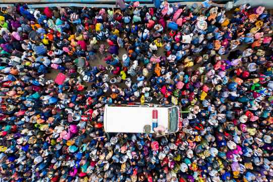Aerial view of a dense crowd of people surrounding a white vehicle, their colorful clothing creating a vibrant mosaic, Mawa, Dhaka Division, Bangladesh.