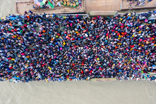Aerial view of a dense crowd of people congregating on a bridge, a vibrant tapestry of colors against the muted tones of the surrounding water, Mawa, Dhaka Division, Bangladesh.