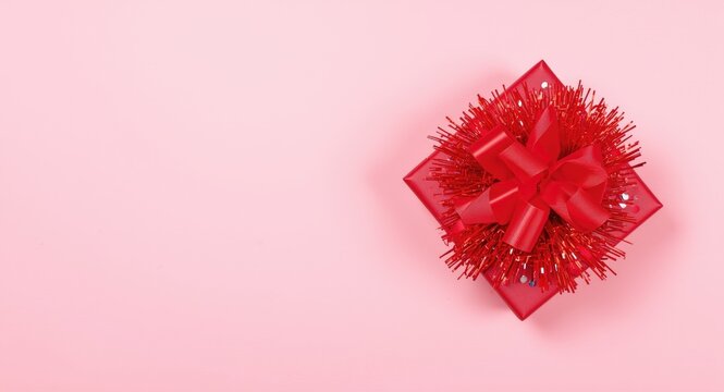 Overhead view of a red present box decorated with sequins tinsel and a bright red bow on a soft pink background with copy space