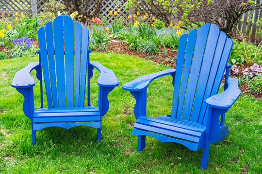 A pair of Adirondack lawn chairs sitting on the lawn in a backyard spring garden.
