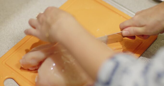 A woman with jewelry cuts a chicken carcass on an orange chopping board