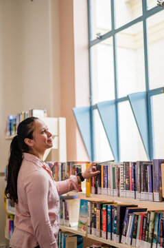 Woman standing in front of a bookshelf reaching for a book in the library