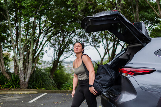 Mixed race woman carrying sports bag from open car boot at parking area