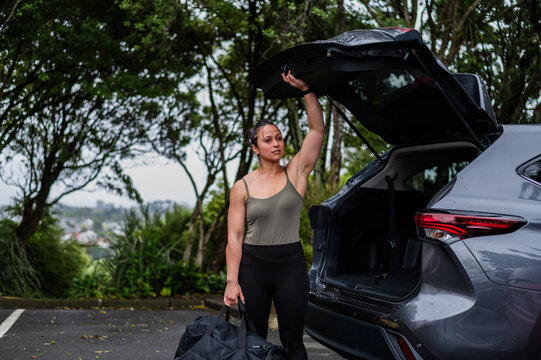 Mixed race woman carrying sports bag while closing car boot at parking area