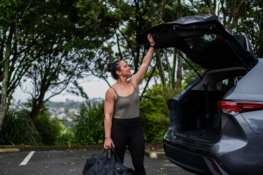 Mixed race woman carrying sports bag while closing car boot at parking area