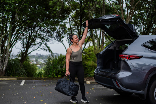 Mixed race woman carrying sports bag while closing car boot at parking area