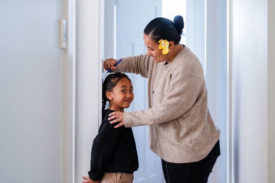 Young Samoan boy with braided hair standing against the wall while mum measures his height