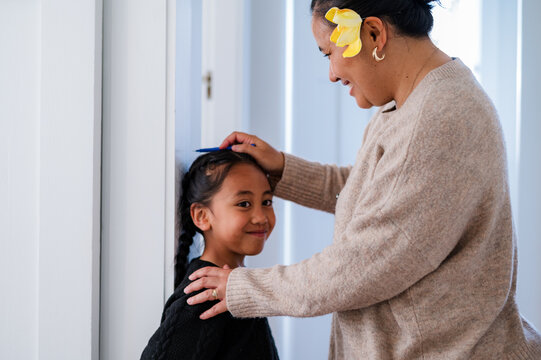 Young Samoan boy with braided hair standing against the wall while mum measures his height