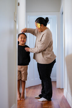 Young Samoan boy with braided hair standing against the wall while mum measures his height