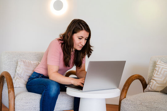 Italian woman sitting on a lounge chair working on her laptop inside home