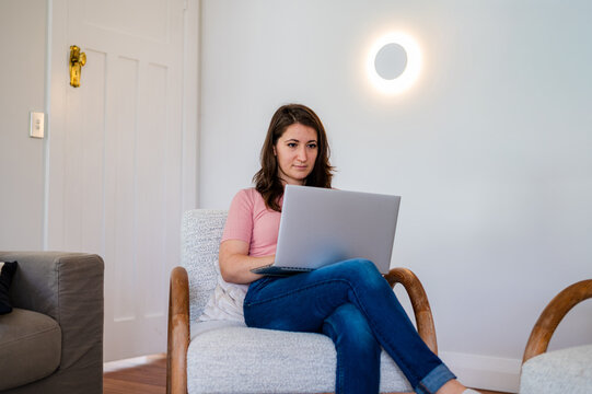 Italian woman sitting on a lounge chair working on her laptop inside home