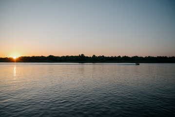Naklejka premium A man on a jet ski sails down a river against the backdrop of the setting sun.