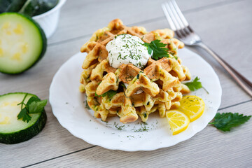 savory zucchini waffles with sour cream and fresh herbs on plate