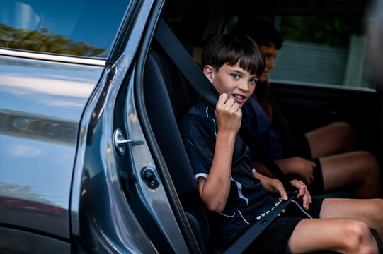 Young boy seated on backseat with other brother fastening his seatbelt