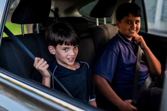 Young boy seated on backseat with older brother fastening their seatbelts