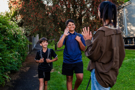 Two boys walking on paved path and waving at mum