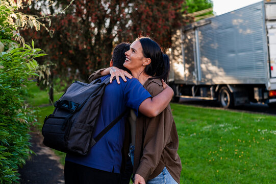 Maori mum hugging teenage son wearing backpack on paved pathway outdoors