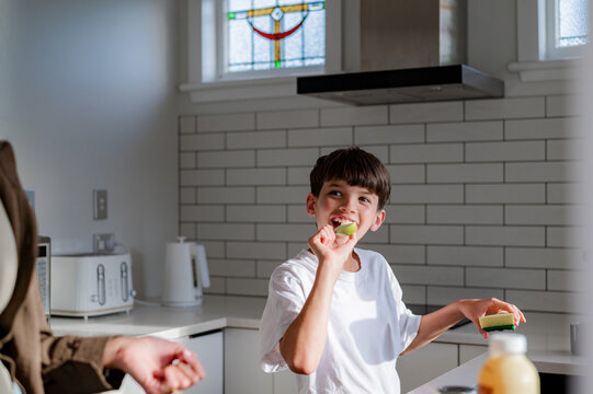 Tween boy eating a slice of green apple in the kitchen looking at mum