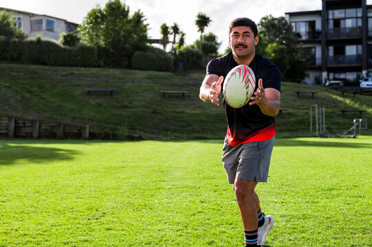 Samoan man practices catching a rugby ball in a grassy park
