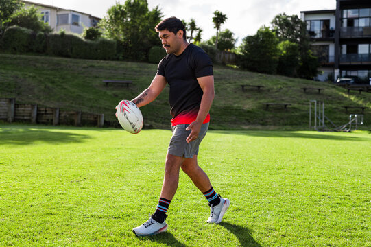 Samoan rugby player holding rugby ball walking on a sunny afternoon at a local field