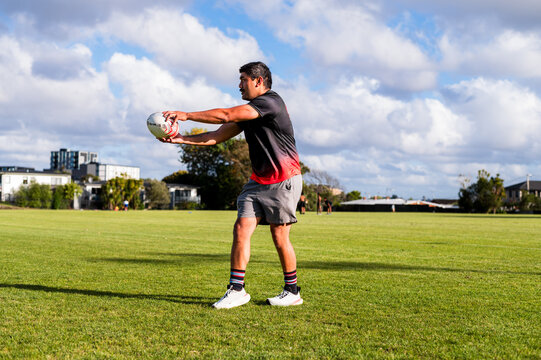 Samoan man trains on a grassy field, skilfully learning to pass a rugby ball under a blue sky