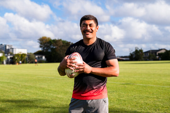 Samoan rugby player smiles while holding a ball at a training session in a green park