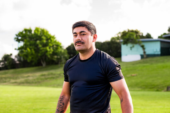 man with a moustache is walking on a sports field wearing a black shirt