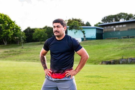 Samoan man doing haka dance moves with arms on his waist in grass field