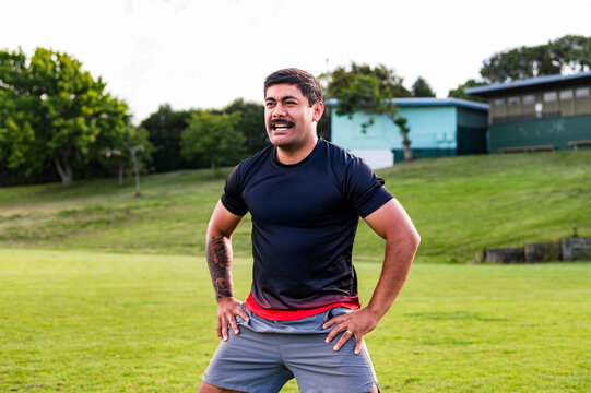Samoan man doing haka dance moves with arms on his waist in grass field