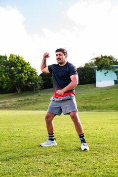 Samoan man doing haka dance moves with one arm lifted in grass field