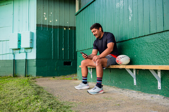 Samoan rugby player sitting on wooden bench holding a phone