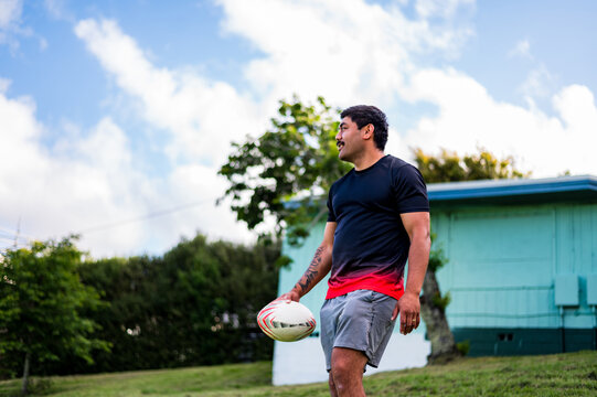 A male rugby player walking down with a ball in a green park under blue skies