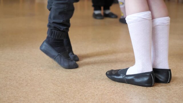 Low angle view preschool students performing rhythmic dance steps wearing black gymnastic shoes and white socks on linoleum floor during morning physical education lesson inside kindergarten hall.